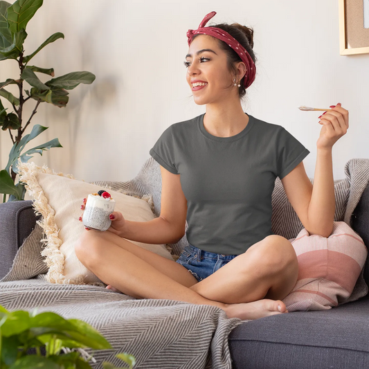 Woman sitting on a couch holding a mug and a cigarette, with plants around her.