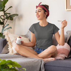 Woman sitting on a couch holding a mug and a cigarette, with plants around her.