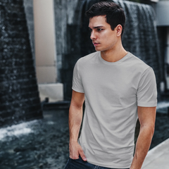 Man wearing a gray t-shirt and dark jeans standing in front of a water fountain.