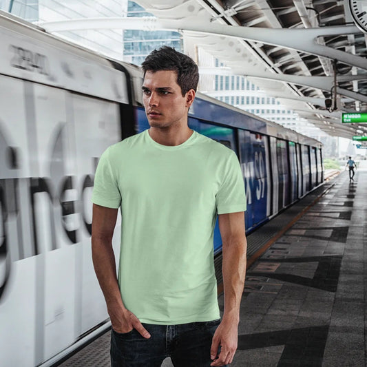 Man wearing a light green t-shirt standing in a train station with a blurred train in the background.