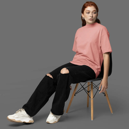 Person sitting on a chair wearing a pink shirt and black pants against a gray background