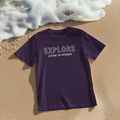 Purple t-shirt with 'EXPLORE EXPLORE THE OUTDOORS' text on sand with ocean waves in background