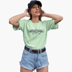 Woman wearing a light green t-shirt with 'Outdoor Adventure' text, blue shorts, and a black cap on a white background