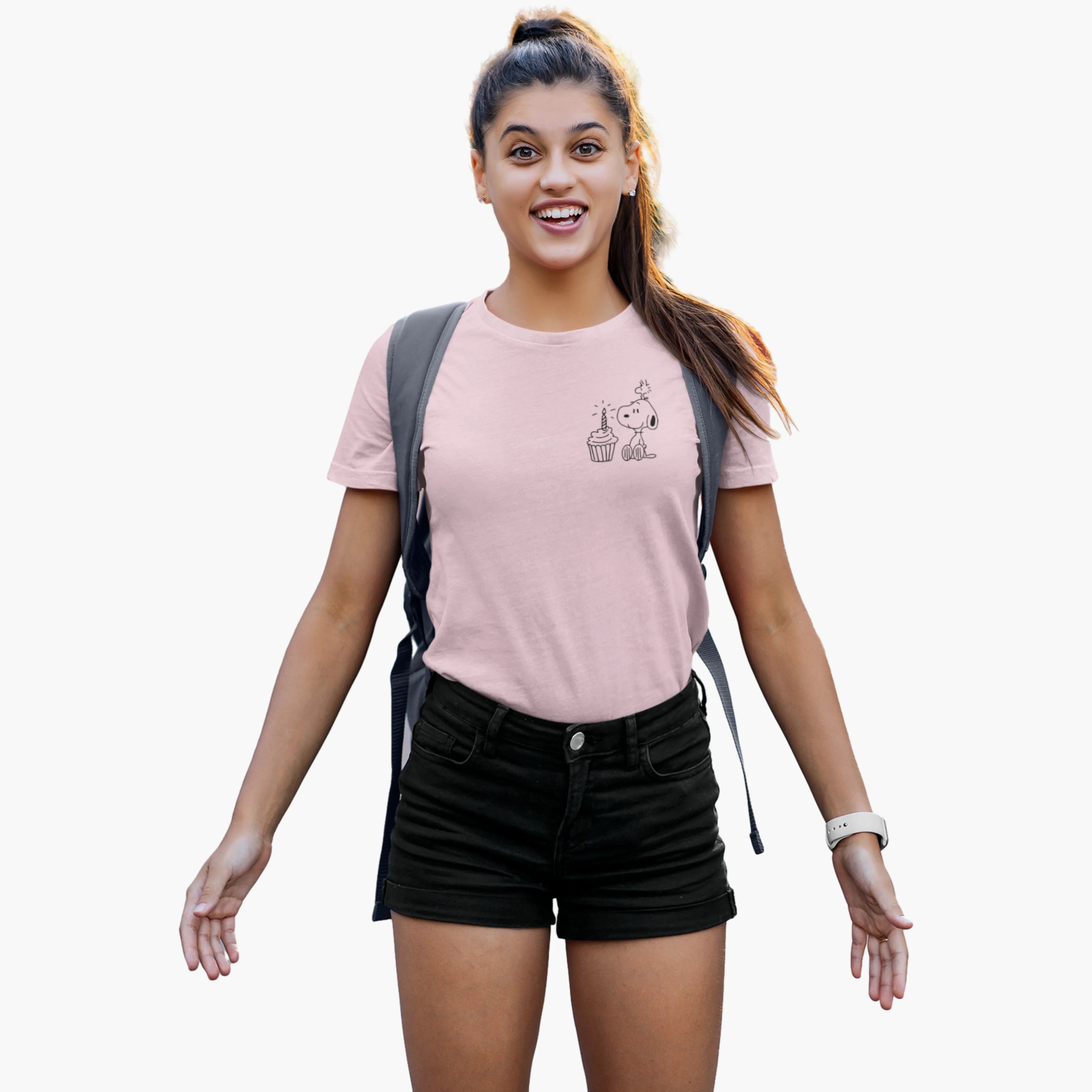 Woman wearing a pink t-shirt with a graphic design and black shorts, standing against a white background.