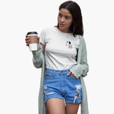 Woman wearing a white t-shirt with a design, blue shorts, and a green cardigan holding a coffee cup.