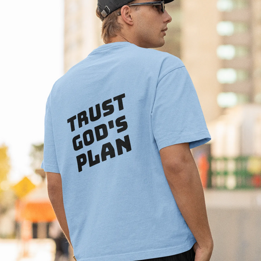 Person wearing a light blue t-shirt with 'Trust God's Plan' text on the back, standing outdoors.