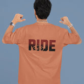 Person wearing a brown t-shirt with 'RIDE' printed on the back against a blue background