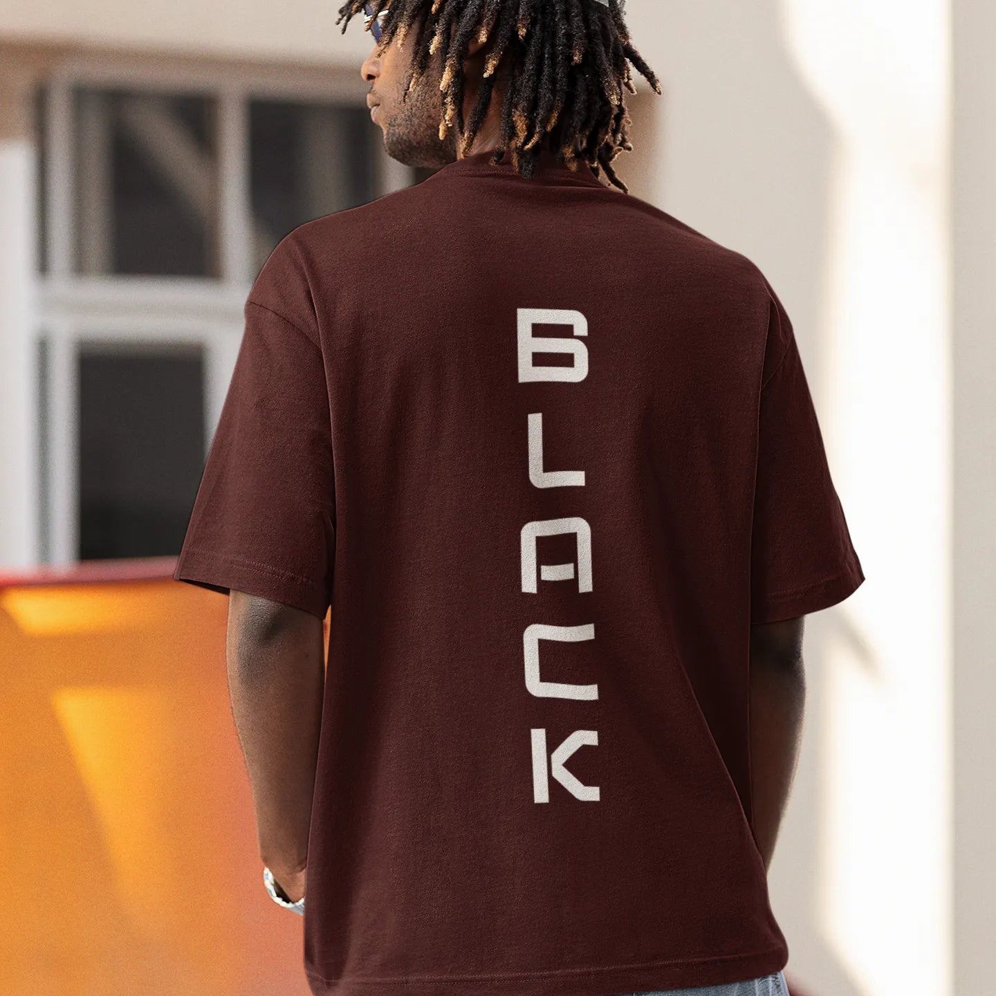 Person wearing a brown t-shirt with 'BLACK' printed vertically on the back, standing outdoors.