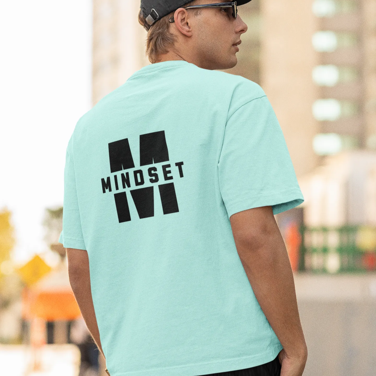 Person wearing a light blue t-shirt with 'MINDSET' printed on the back, standing outdoors.