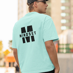 Person wearing a light blue t-shirt with 'MINDSET' printed on the back, standing outdoors.