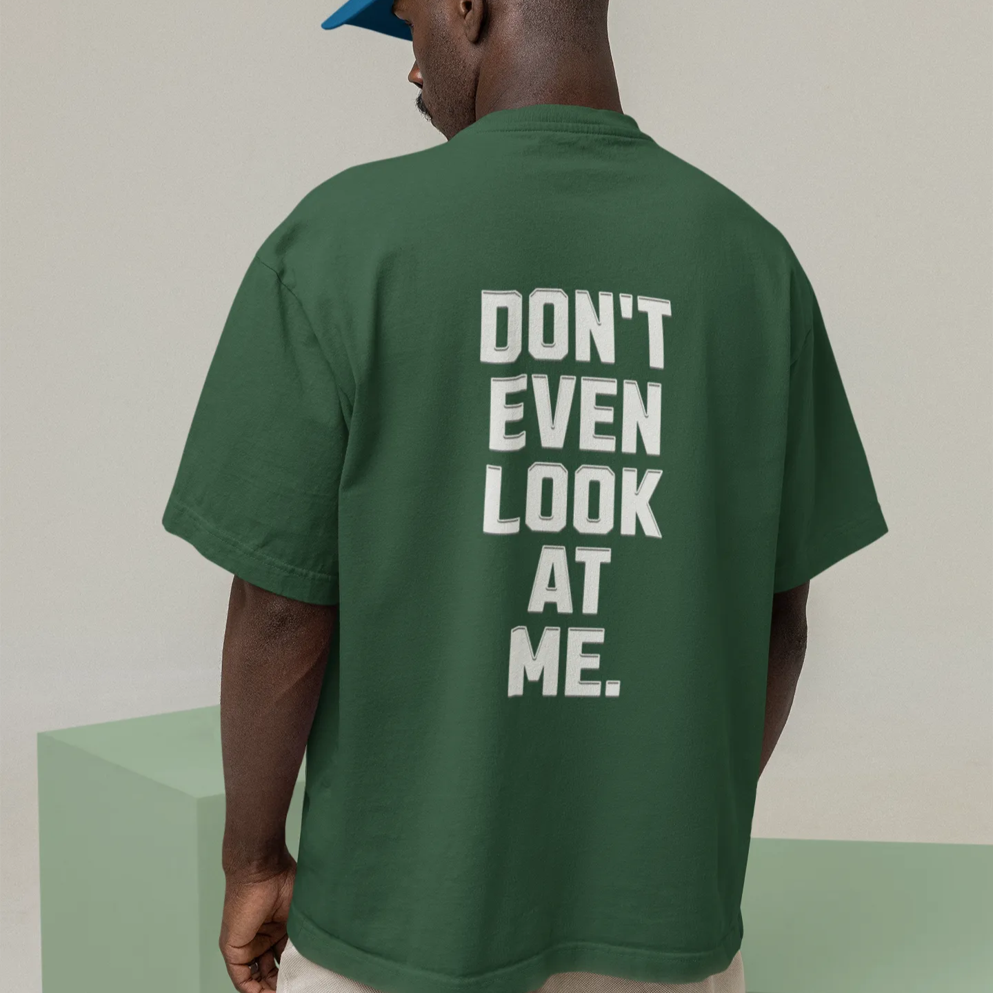 Person wearing a green t-shirt with 'DON'T EVEN LOOK AT ME' text on the back, standing against a plain background.