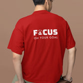 Person wearing a red t-shirt with 'FOCUS ON YOUR GOAL' text on the back against a brown background