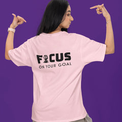Person wearing a pink t-shirt with 'FOCUS ON YOUR GOAL' text on the back against a purple background