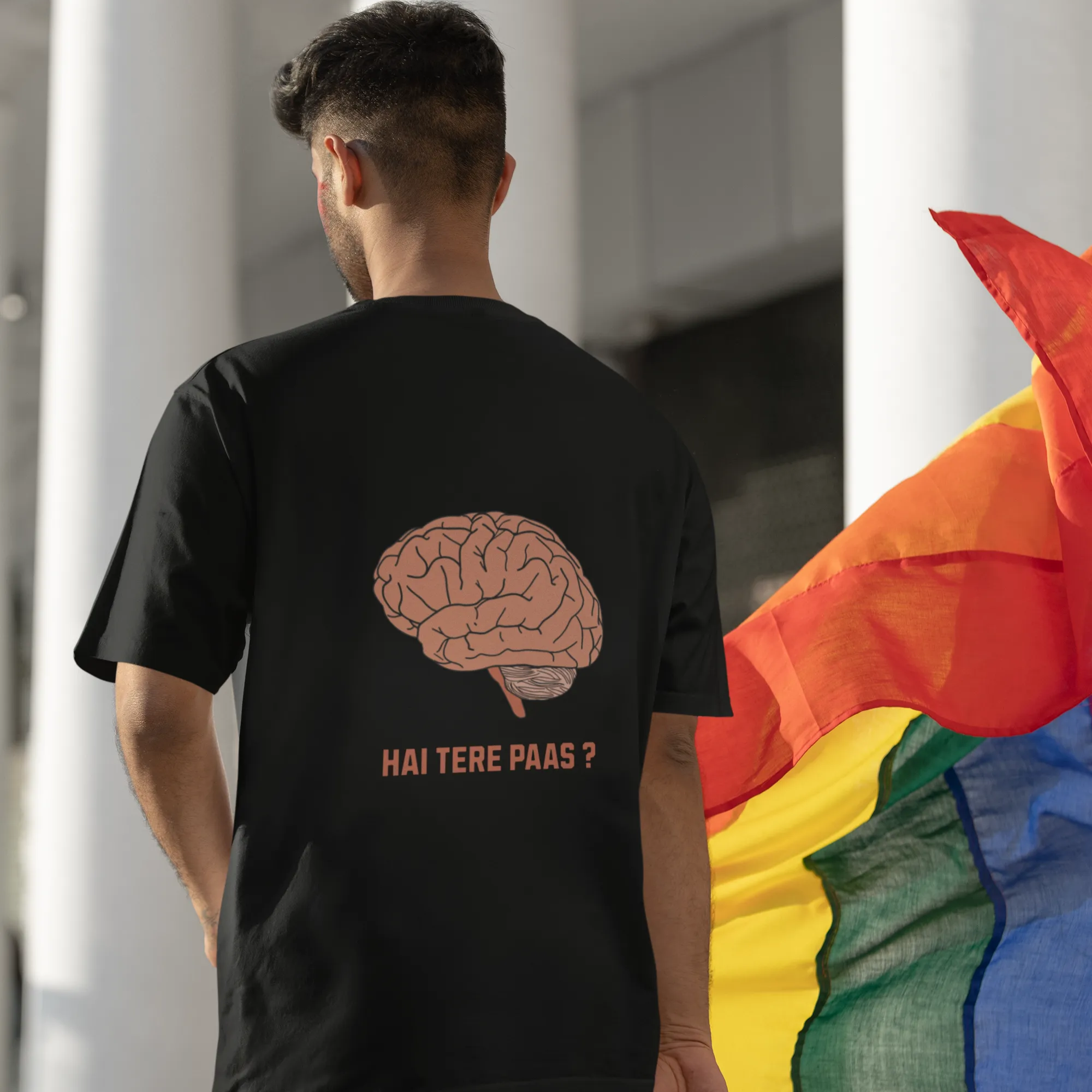 Person wearing a black t-shirt with a brain graphic and text, standing next to a rainbow flag.