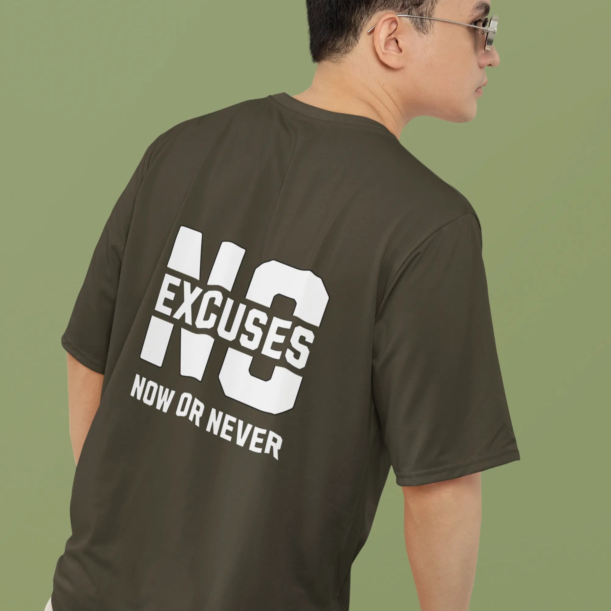 Man wearing a green t-shirt with 'NO EXCUSES NOW OR NEVER' text on the back against a green background