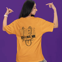 Person wearing a mustard yellow t-shirt with text on the back against a purple background