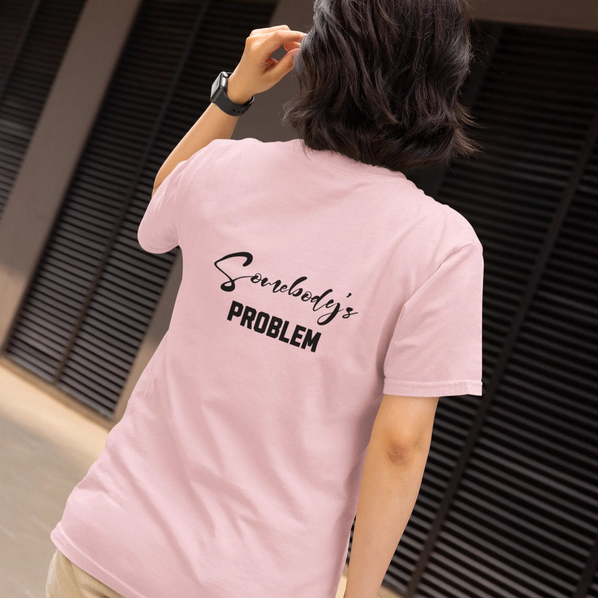 Person wearing a pink t-shirt with text on the back, standing in front of a building.