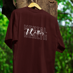 Maroon t-shirt with 'Mental Health Matters' text on a hanger against a tree background