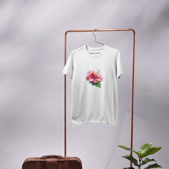 White t-shirt with a floral design on a copper rack, next to a brown suitcase and potted plant.