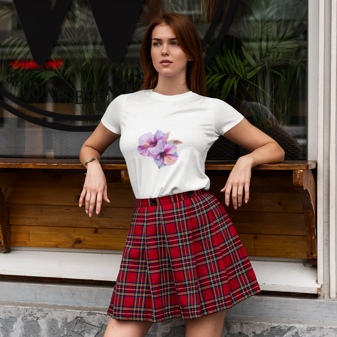 Woman wearing a white t-shirt with a floral design and a red plaid skirt sitting on a wooden bench.