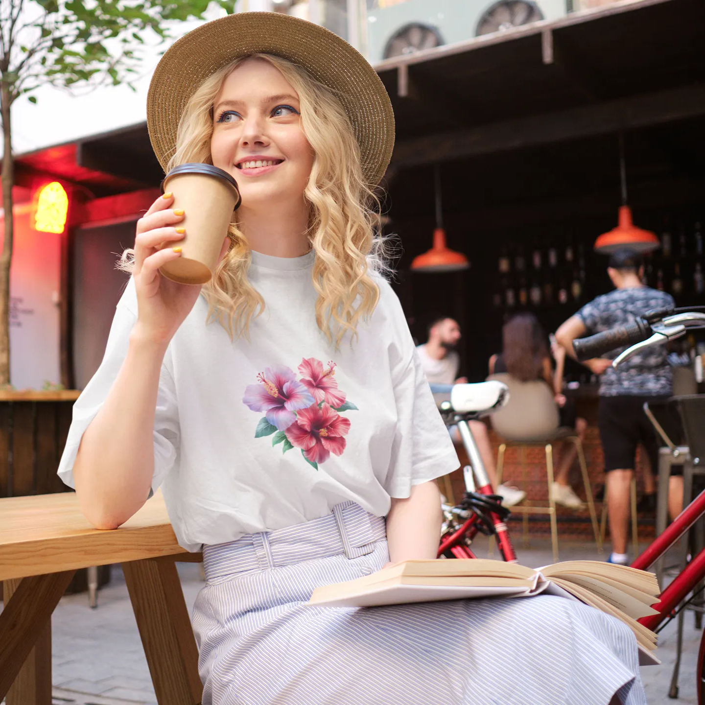 Woman sitting at a outdoor cafe, holding a drink and reading a book.