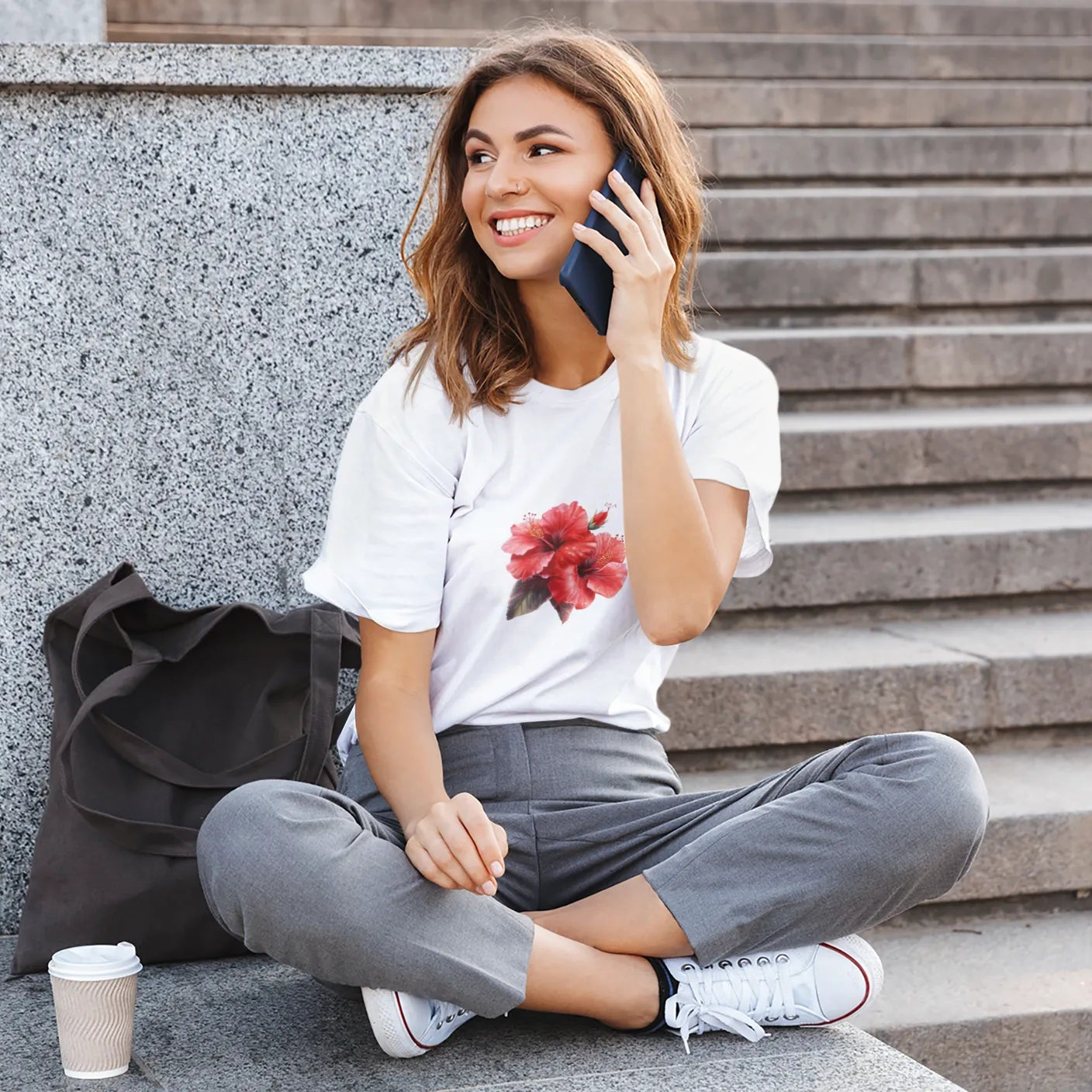 Woman sitting on steps talking on a phone with a coffee cup nearby