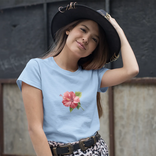 Woman wearing a light blue t-shirt with a floral design and a black hat, standing against a textured wall.