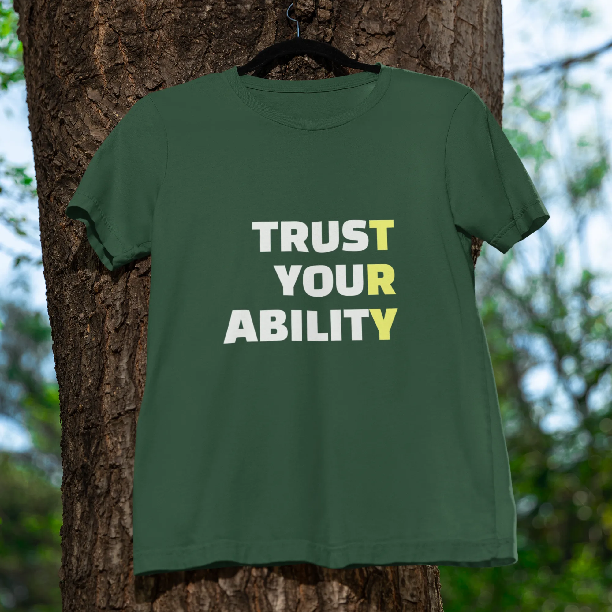 Green t-shirt with 'Trust Your Ability' text hanging on a tree