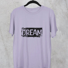 Lavender t-shirt with 'DREAM' print on a hanger against a gray concrete wall.