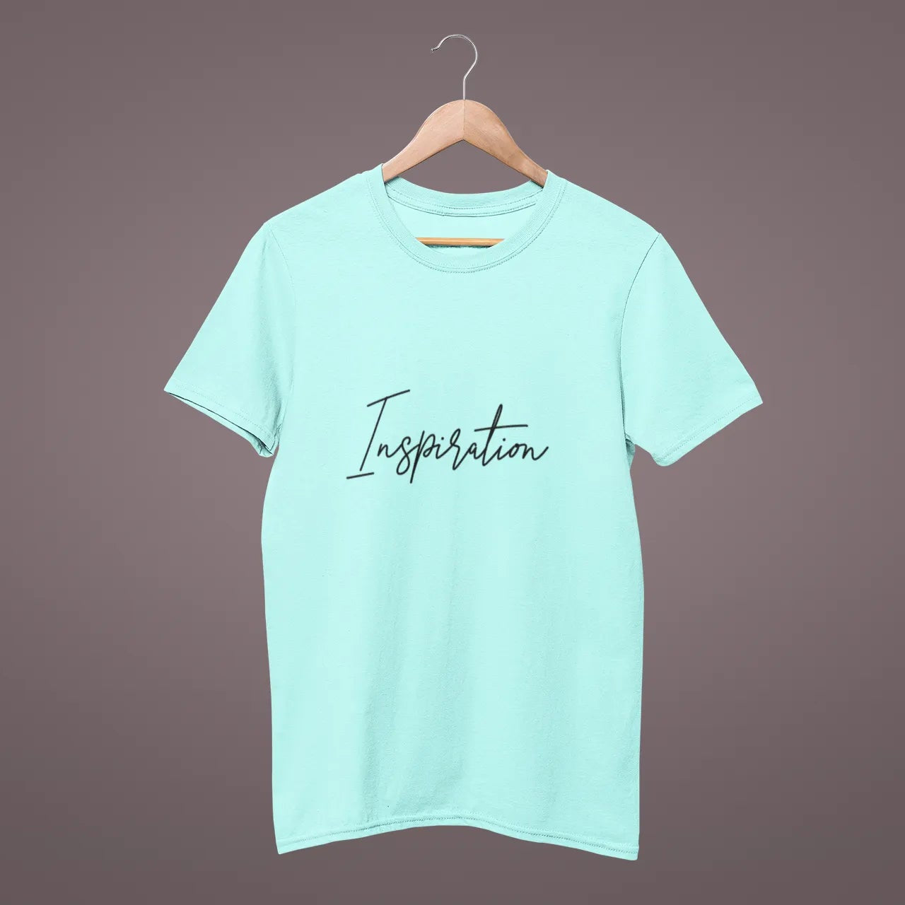 Mint green t-shirt with 'Inspiration' text on a hanger against a dark background