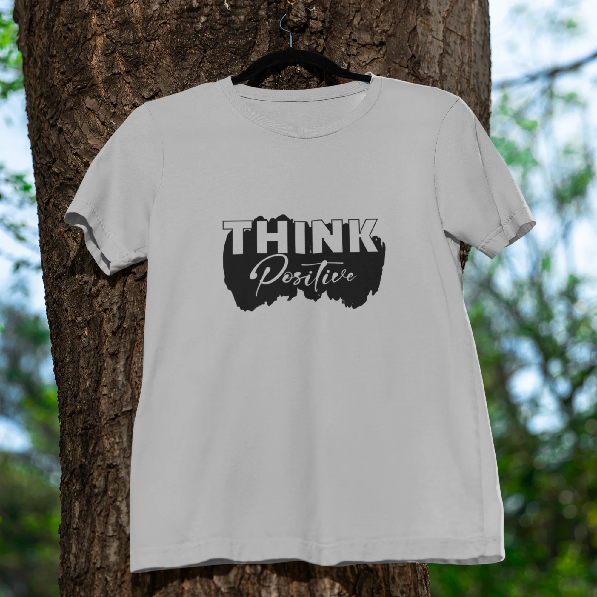 White t-shirt with 'Think Positive' text on a tree trunk