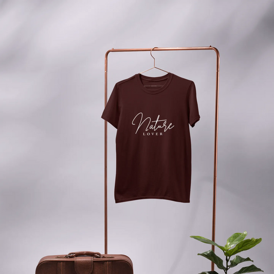 Brown t-shirt with 'Nature Lover' text on a hanger, next to a brown suitcase and potted plant on a gray background