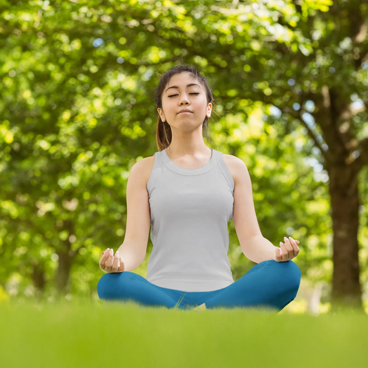 Woman meditating in a park with green trees and grass.