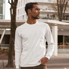 Man wearing a white long-sleeve shirt standing outdoors with modern buildings in the background