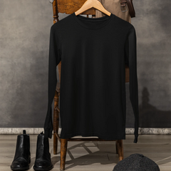 Black long-sleeve shirt on a wooden chair with black boots and a cap on the floor against a gray wall.