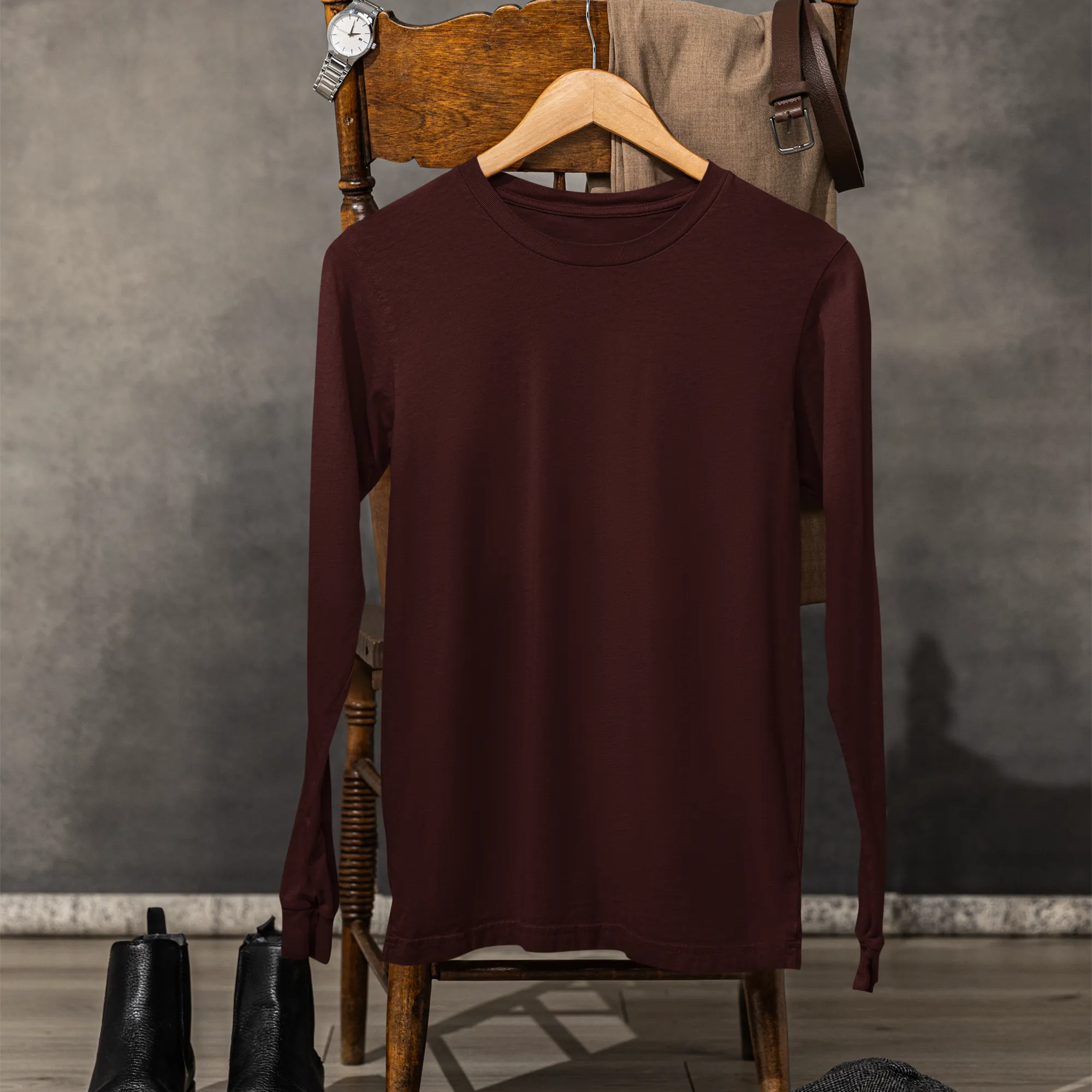 Brown sweater on a wooden chair with black boots and a gray cap on a wooden floor.