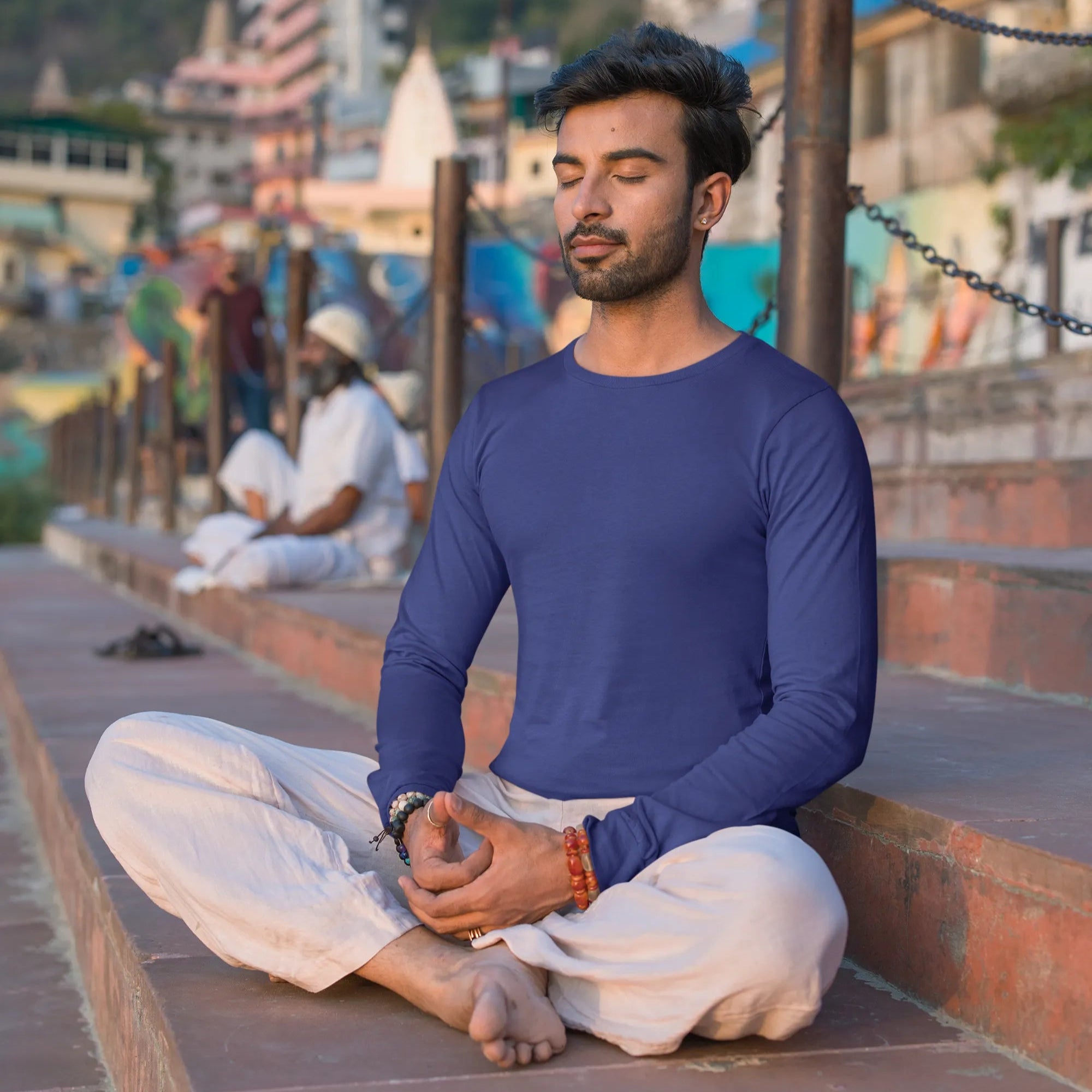 Man meditating in a serene outdoor setting with mountains and buildings in the background