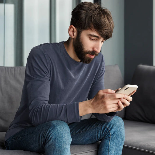 Man sitting on a couch using a smartphone in a modern living room.