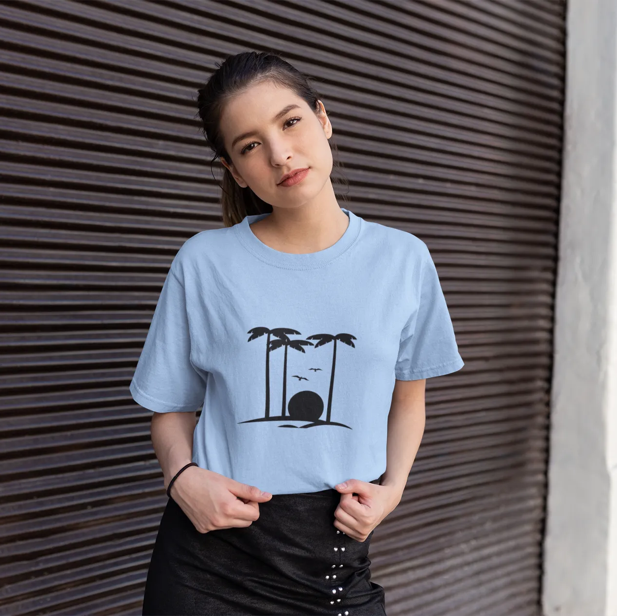 Woman wearing a light blue t-shirt with a graphic design, standing against a textured wall.