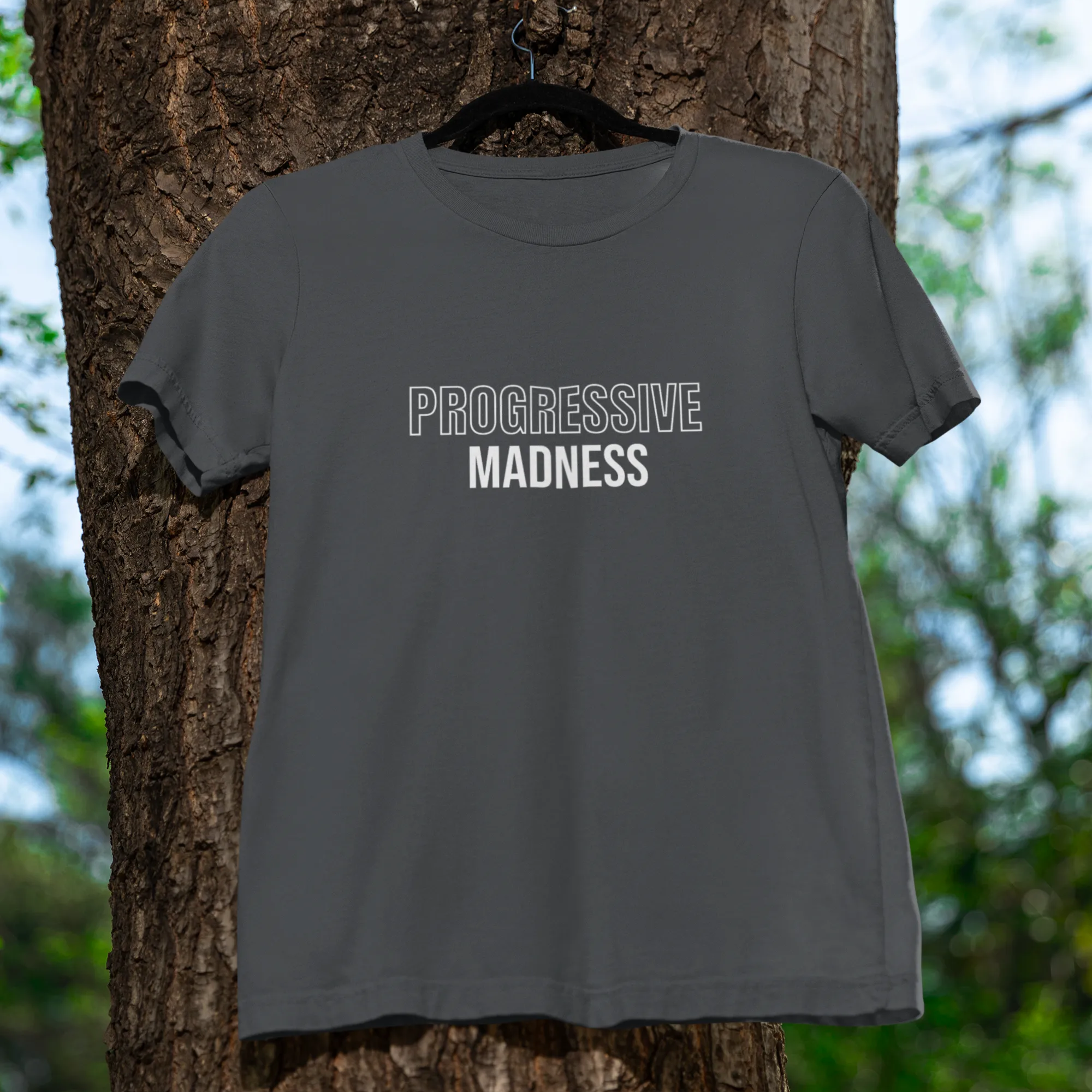 Gray t-shirt with 'PROGRESSIVE MADNESS' text hanging on a tree
