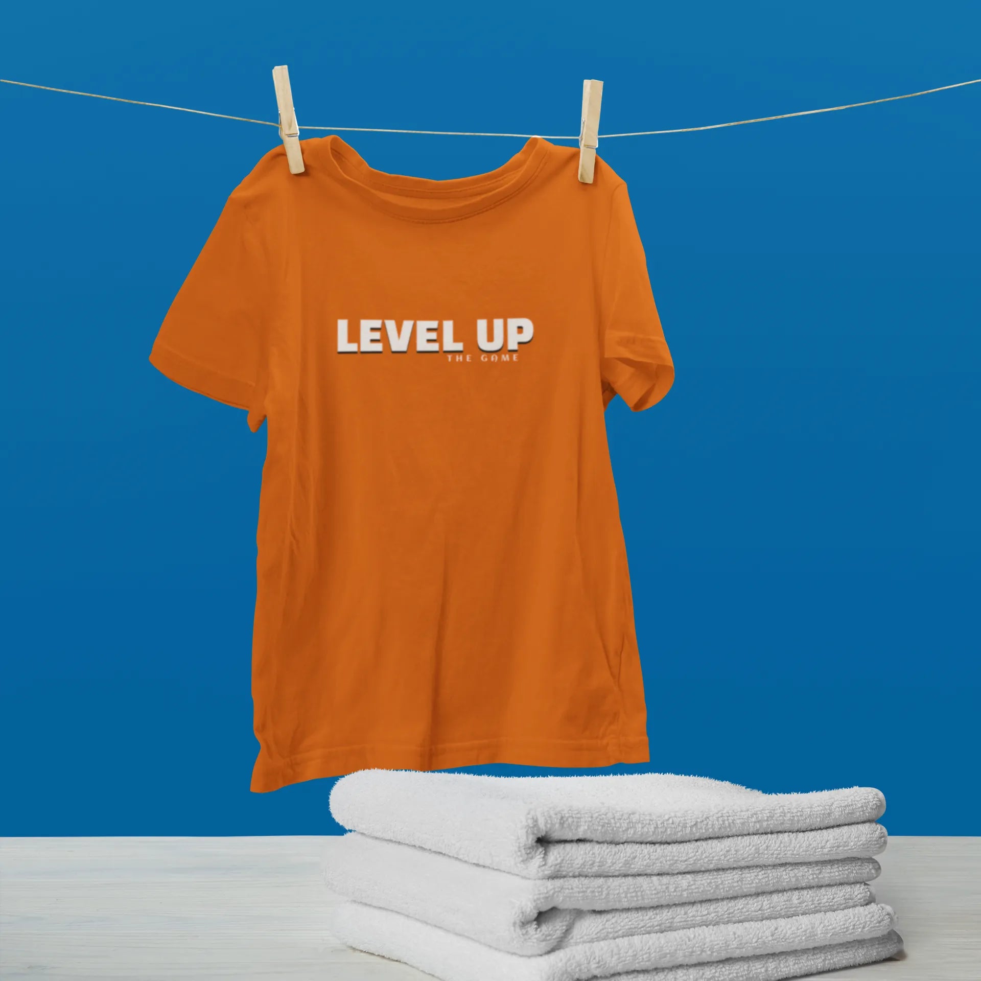 Orange t-shirt with 'LEVEL UP' text on a clothesline against a blue background