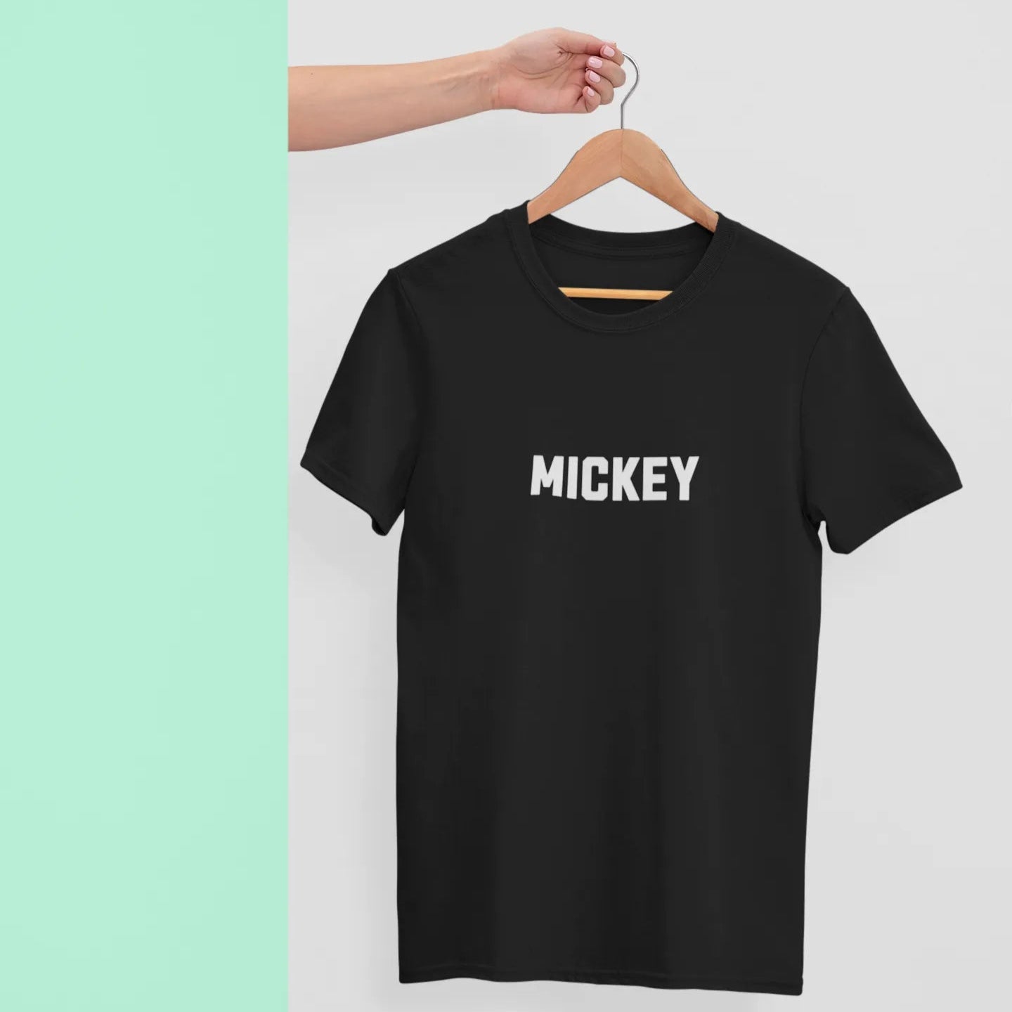 Black t-shirt with 'MICKEY' text on a hanger against a light green background