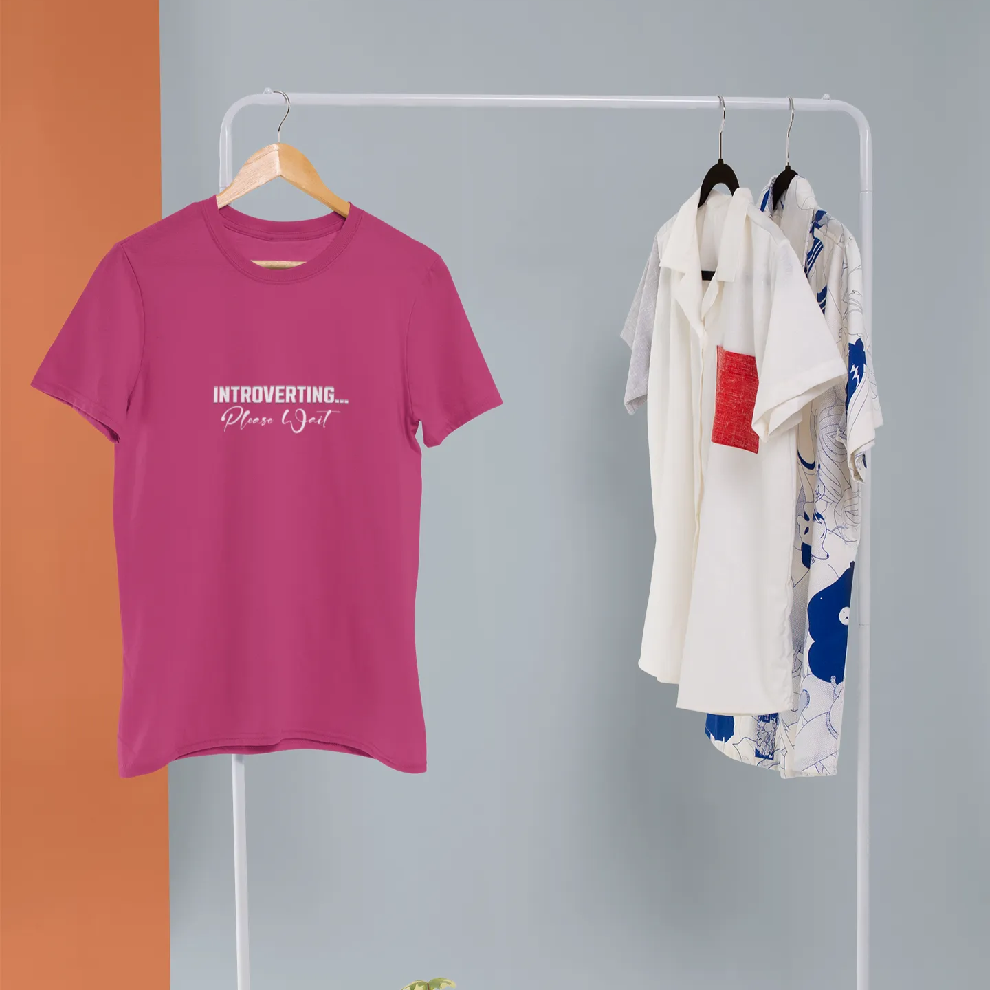 Pink t-shirt with text on a white clothing rack against a gray wall.