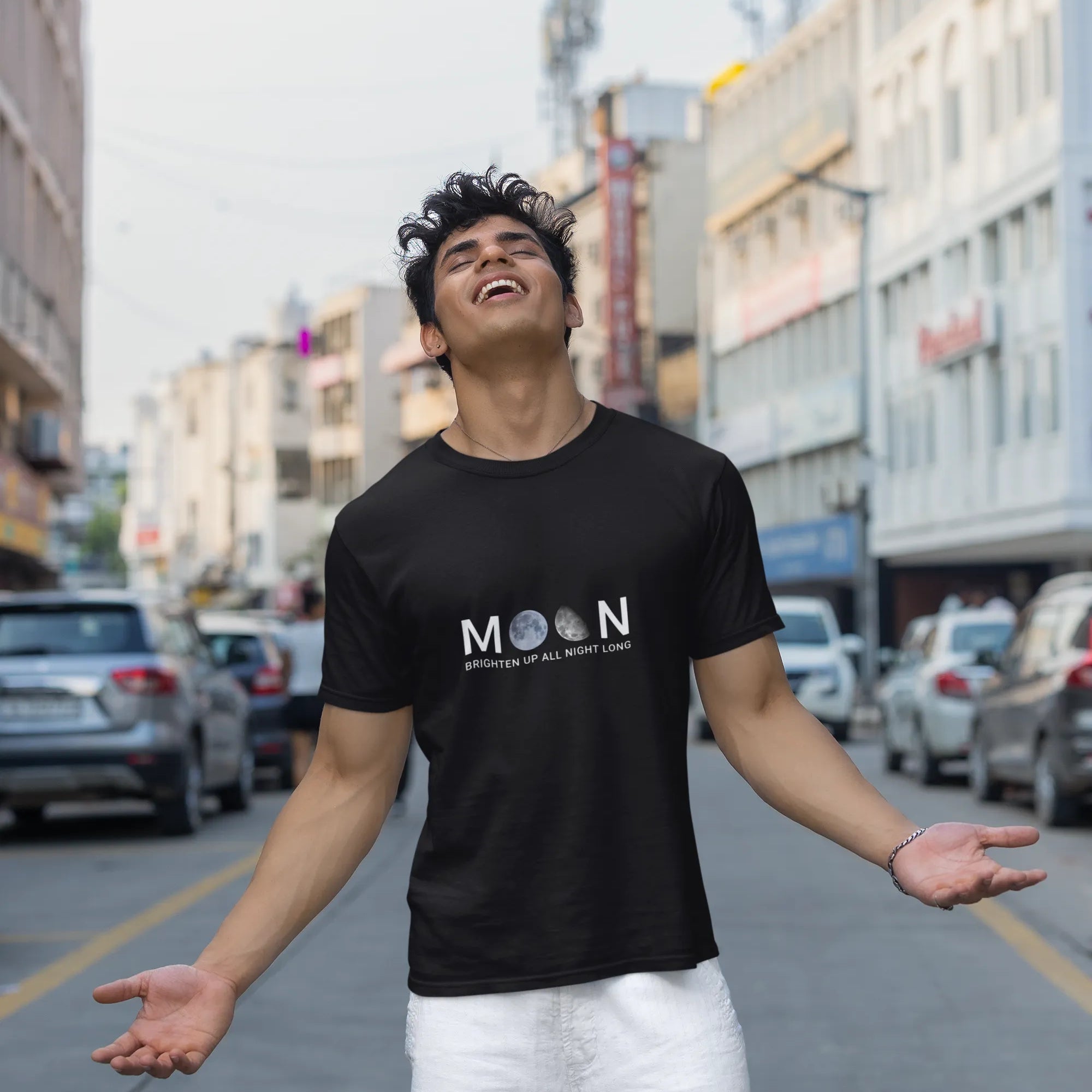 Person wearing a black t-shirt with 'MOON' logo on a city street