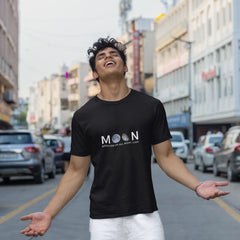 Person wearing a black t-shirt with 'MOON' logo on a city street