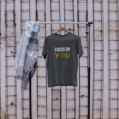 T-shirt with 'Focus on You' text, jeans, and sneakers on a stand against a textured wall.