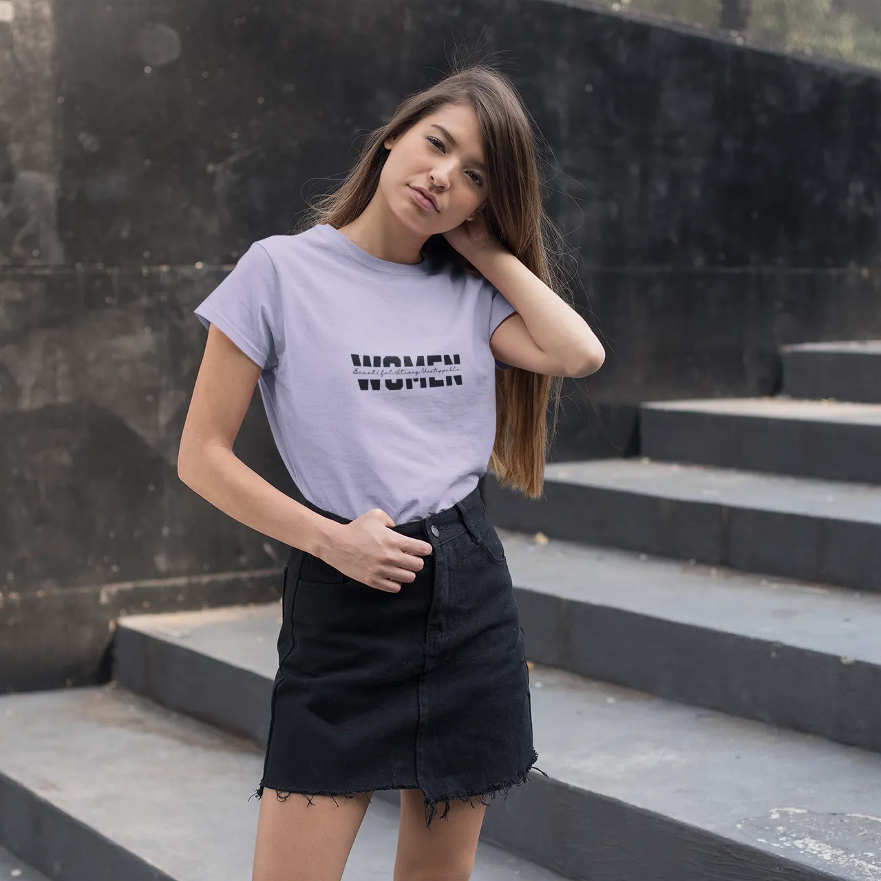 Woman wearing a light purple t-shirt with text on it, standing on steps against a dark wall.