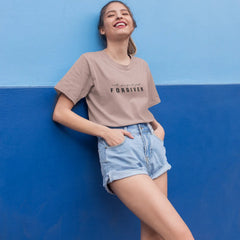 Woman wearing a beige t-shirt with text and denim shorts against a blue wall.
