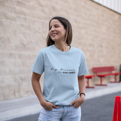 Woman wearing a light blue t-shirt with text, standing outdoors near a building.