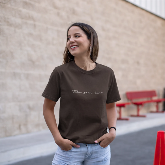 Woman wearing a brown t-shirt with text, standing outdoors near a building.